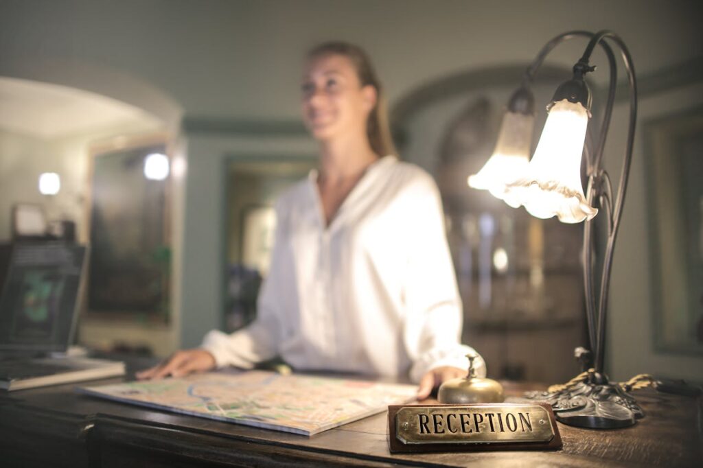 pexels-photo-3771811-1 A concierge stands at a hotel reception desk under ambient lighting, ready to assist guests.